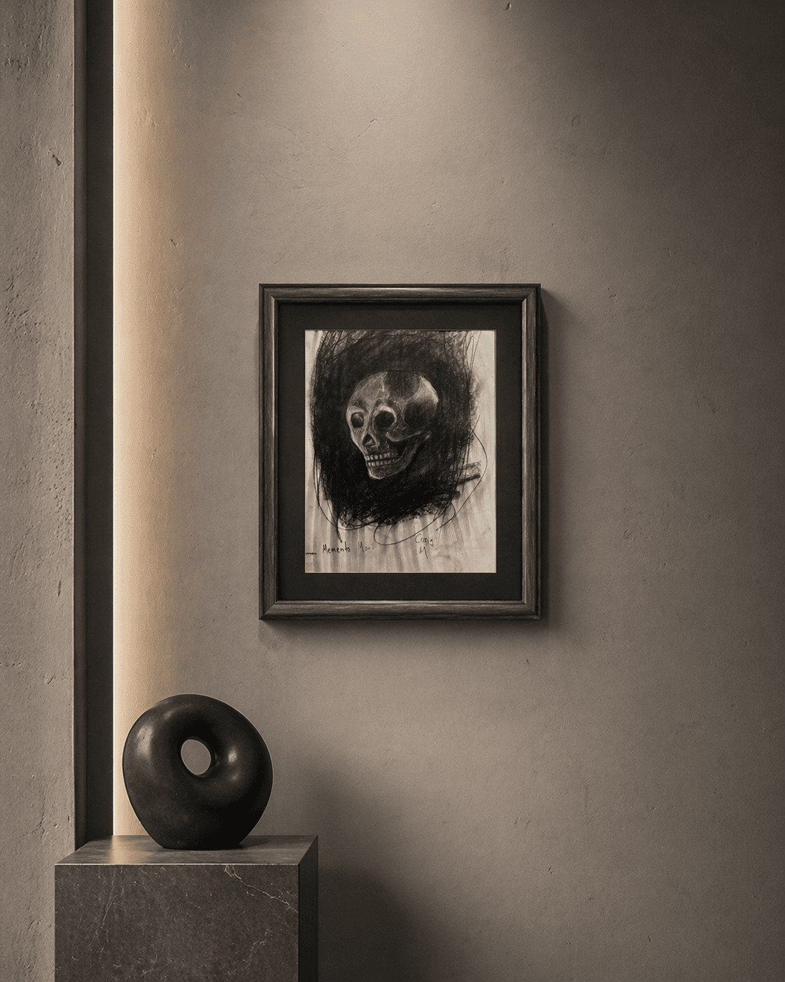 Framed charcoal skull drawing on a wall above a black torus sculpture on a pedestal.