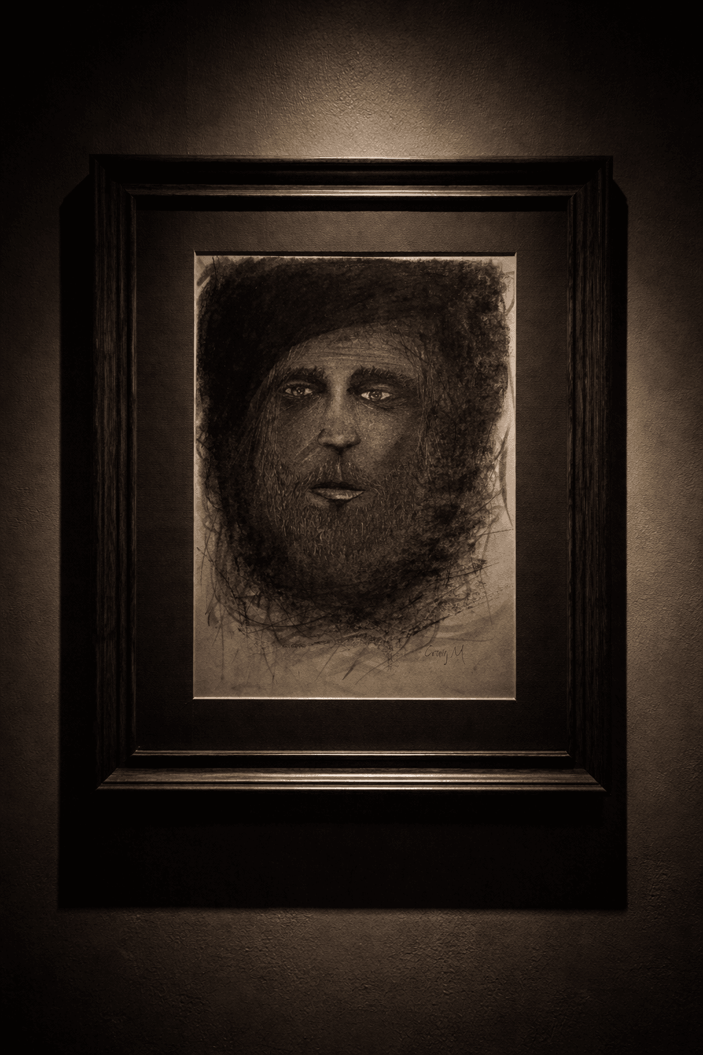 Framed charcoal sketch of a bearded man with intense eyes, spotlighted on a dark wall.